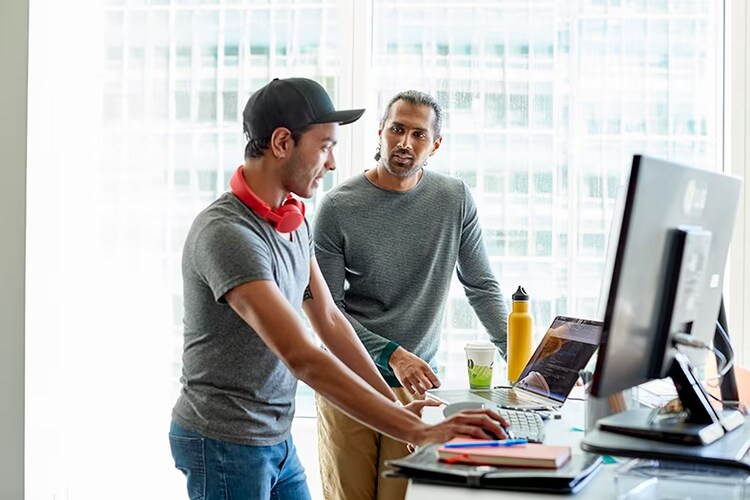 men conversing while standing at their computers