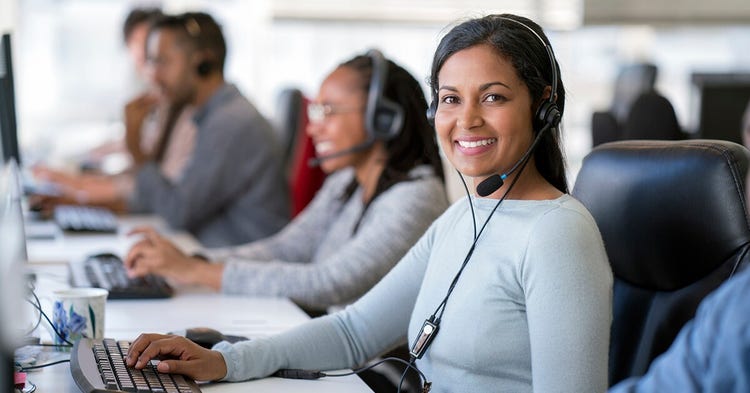 Portrait of smiling businesswoman wearing headset while using computer. Confident female operator is working with colleagues at desk. They are in call center.