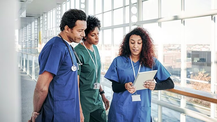 Healthcare employee experience: 3 healthcare workers look at a tablet screen.