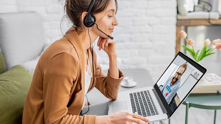 Hybrid work: A woman with a headset on smiles at her colleague on her laptop screen.