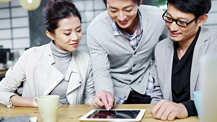 Improving service management: Three employees converse while looking at a tablet.