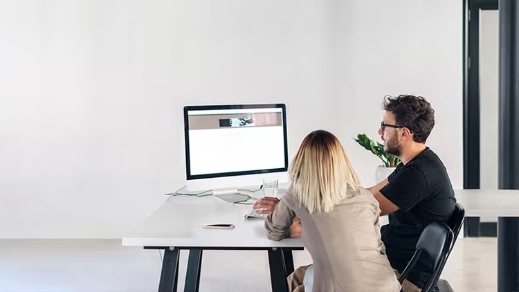 Execution management meets digital workflows: Two employees sit at a desk looking at a computer monitor.