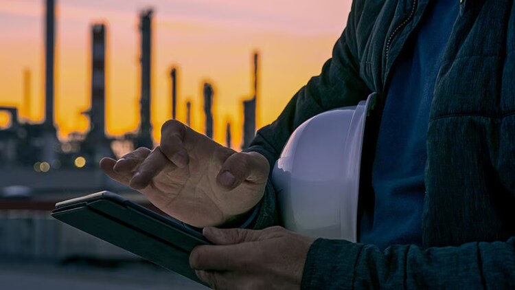A man holds his hard hat while browsing his phone.