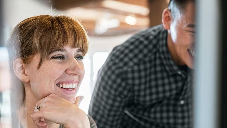 Driving customer experience: A man and woman smile at a computer monitor.