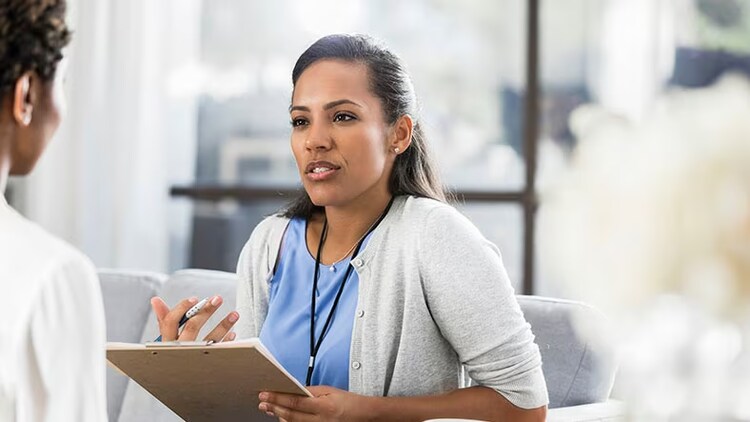 Experiences in healthcare and life sciences: A woman consults with a healthcare worker holding a clipboard.