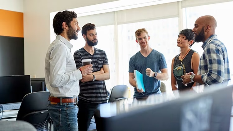 Employee experience: 5 employees stand chatting in an office.