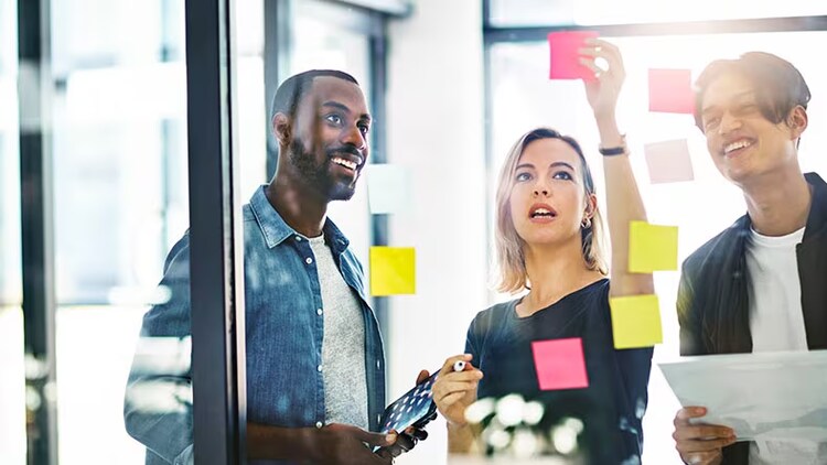 Agile project management: 3 employees discuss a project while posting sticky notes.