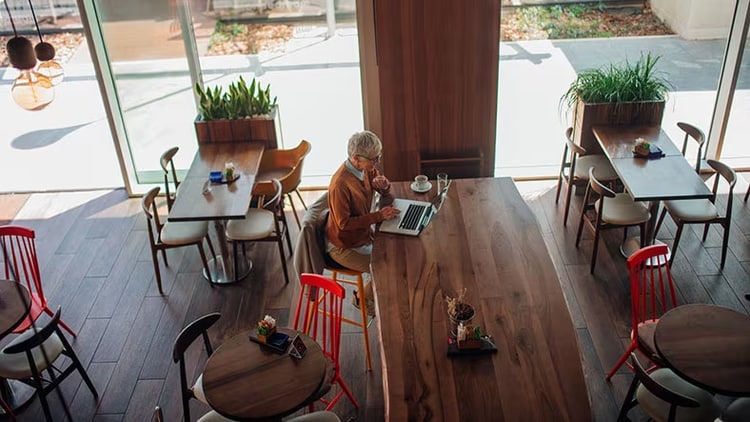 Customer experience: A woman sits at a table in a vacant cafe working on a laptop.