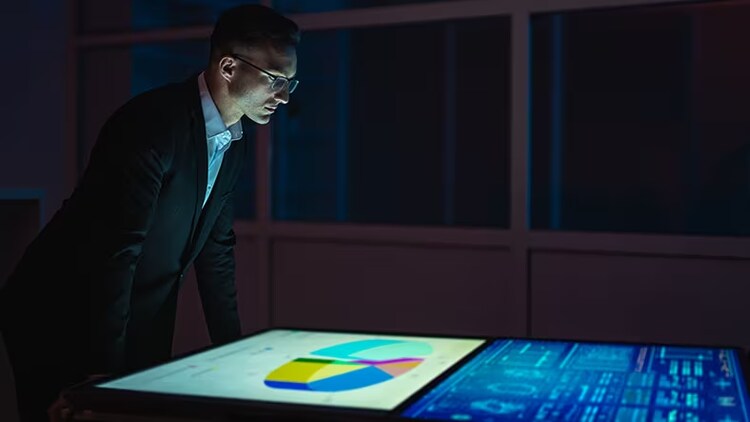 A businessman leans over two large monitors detailing sales analytics.