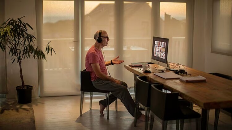 Hybrid work: A businessman sits in his home conversing with fellow employees through his computer screen.