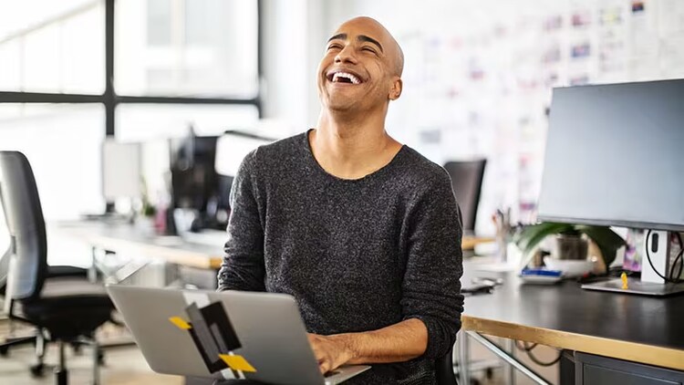 Using all the power of ITSM: A businessman laughs while working on a laptop in an office.