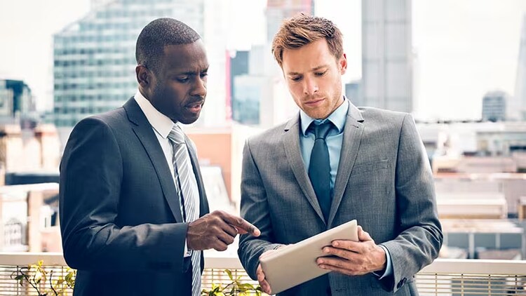 Citizen experience: Two businessmen discuss something on a tablet with city skyscrapers in the background.