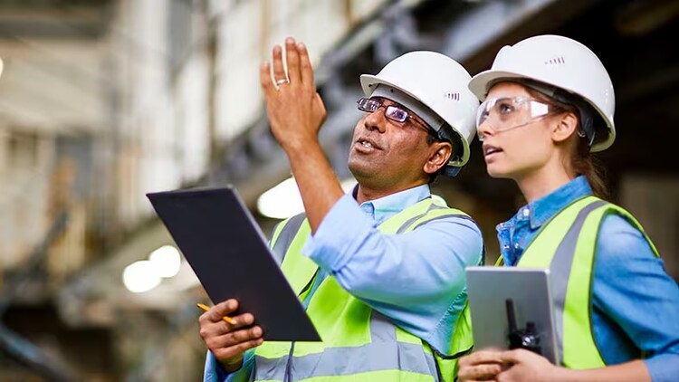 2 manufacturing workers hold tablets and discuss work.