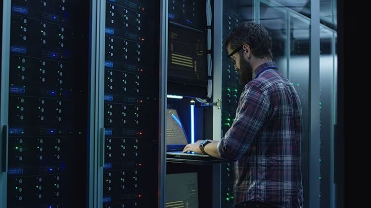 Modernize IT: A businessman works on a laptop in a datacenter server room.