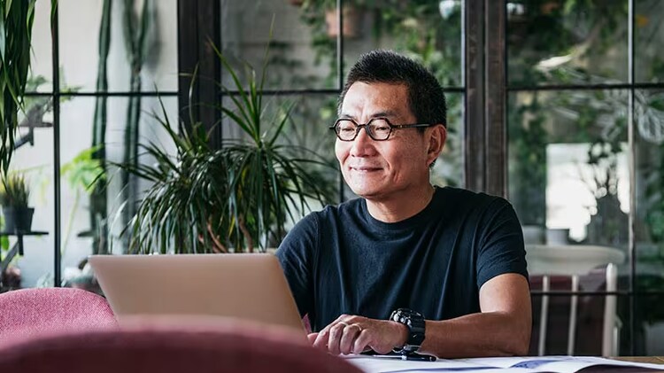Streamlined ERP migrations, modern systems of record: A man sits at a table working on a laptop.