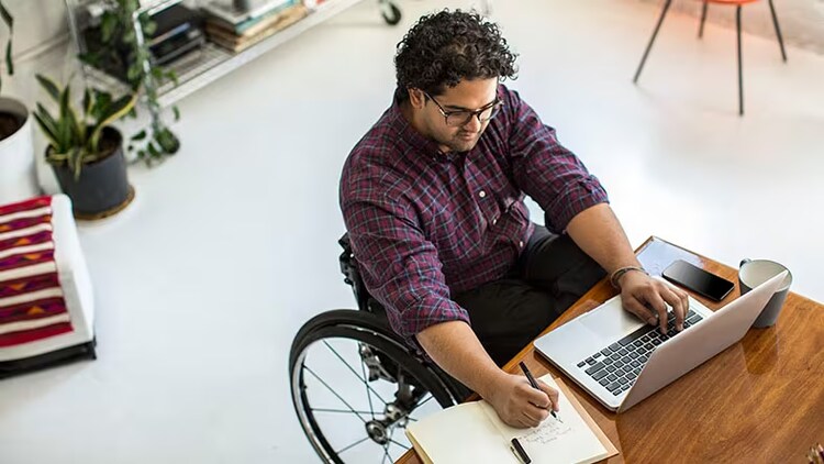 Employee experience: A man in a wheelchair writes in his journal and works on his computer.
