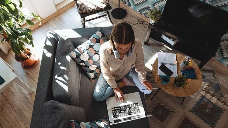 Hybrid work employee experience: A young woman works on a laptop at home.
