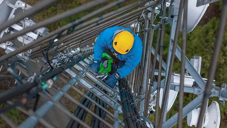 Man with a hard hat climbs a telecommunications tower.