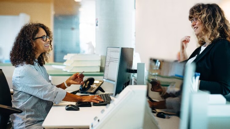 Two women conversing with each other across a desk.