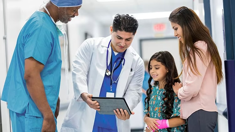 Healthcare: A male doctor and nurse look at a tablet with a young patient and her mother.