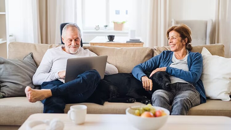 Customer service: A couple sit on their couch with a dog, looking at a laptop.