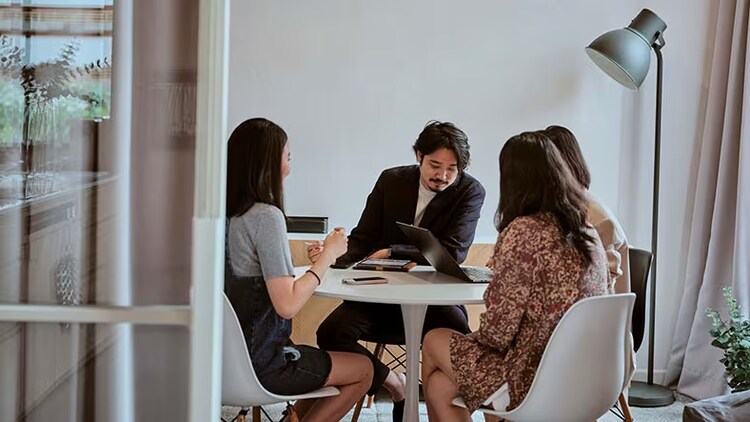NextGen Program helps underrepresented groups get tech jobs: 3 women and 1 man gathered around conference room table and laptop