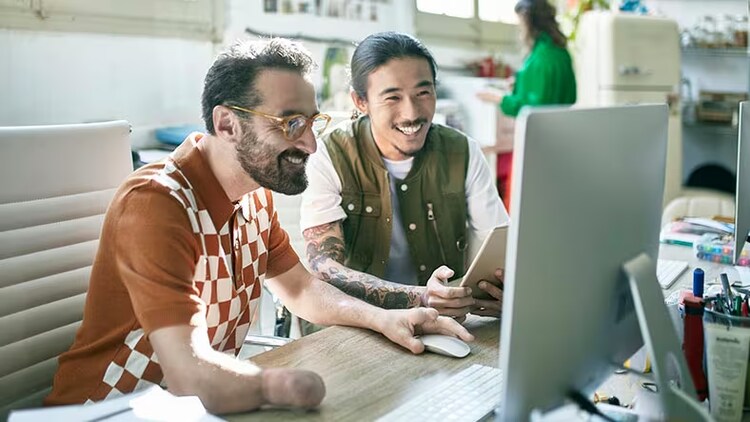 Technology excellence: two co-workers smiling at large Apple computer monitor