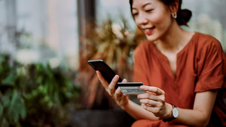 Banking IT support: A woman looks holds a smartphone in one hand and a credit card in the other.
