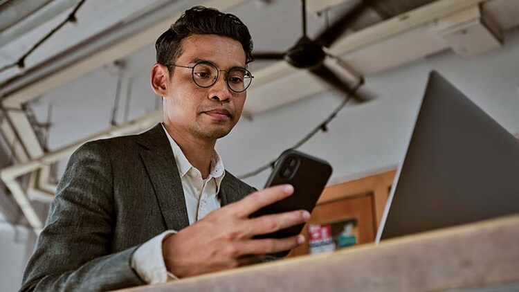 Mobile app adoption: man at a desk in front of laptop looking at phone in his hand