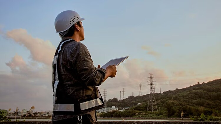 Field service: man in hard with tablet in hands looking at power lines