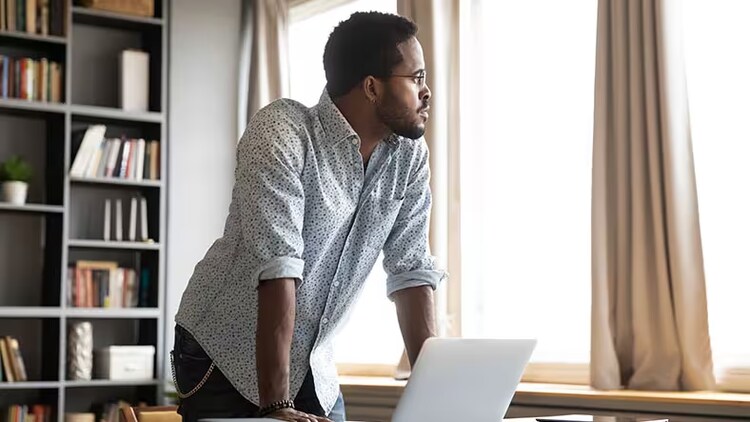 Uncertain times: man standing in front of open laptop looking out a window