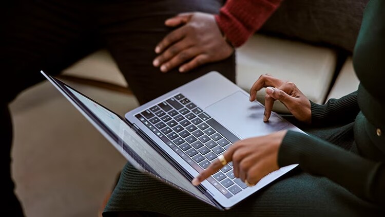 AIOps: One worker points at a laptop screen while another worker looks on.