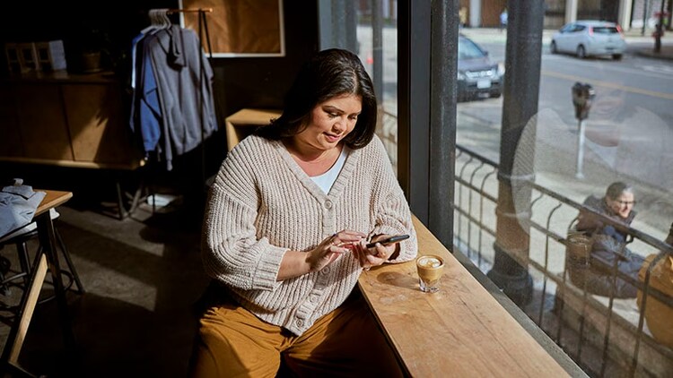Customer experience: A woman looks at her cellphone at a coffee shop.