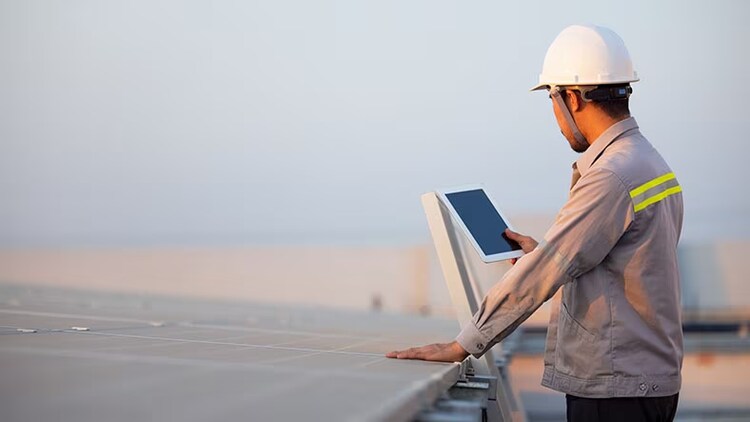 Field service: Man in hard hat looking at solar panels and a tablet