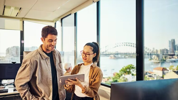 AI and automation: man and woman looking at a tablet in office overlooking Harbor Bridge