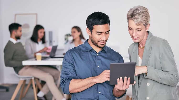 Change enablement: 2 workers looking at a tablet while other workers chat at a table