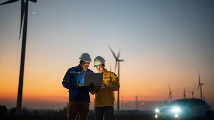AI in field service: 2 field workers looking at a laptop screen in front of windmills
