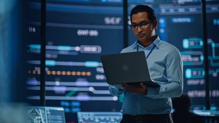 Generative AI: man standing holding an open laptop surrounded by computer screens
