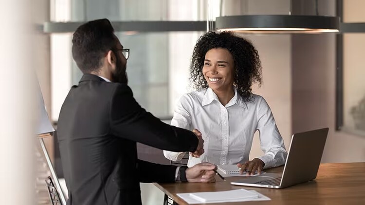 Reimagining the partner experience: 2 seated workers shaking hands in front of an open laptop
