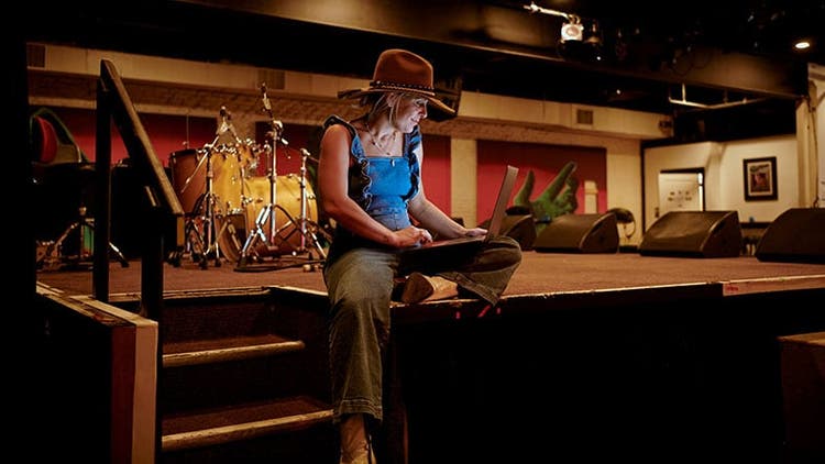 Nontraditional talent: woman in a cowboy hat sitting on stage looking at laptop