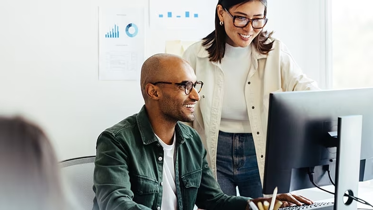 Knowledge-sharing culture: man and woman smile at computer monitor on desk
