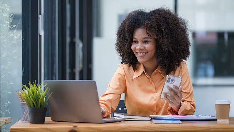 Employee onboarding: smiling worker with phone in hand looking at open laptop on desk