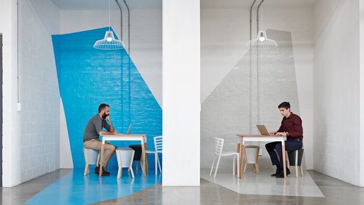 Competition for talent: 2 workers with laptops seated at tables, facing each other, divided by a wall