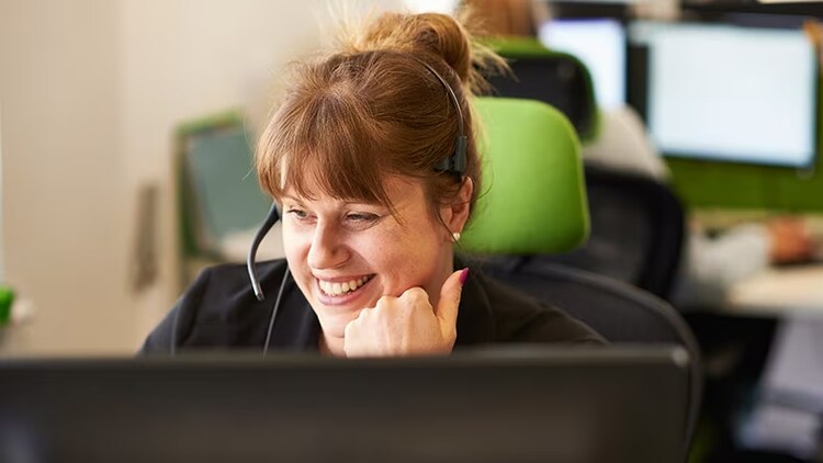 Automated issue response: smiling woman with headset on in front of a computer monitor at an office
