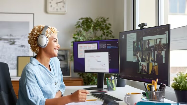 Microsoft Teams apps: woman with headphones smiling at two computer monitors in front of her