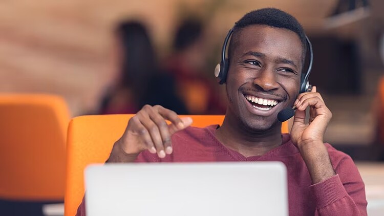 AI in the contact center: smiling male worker wearing headset in front of open laptop