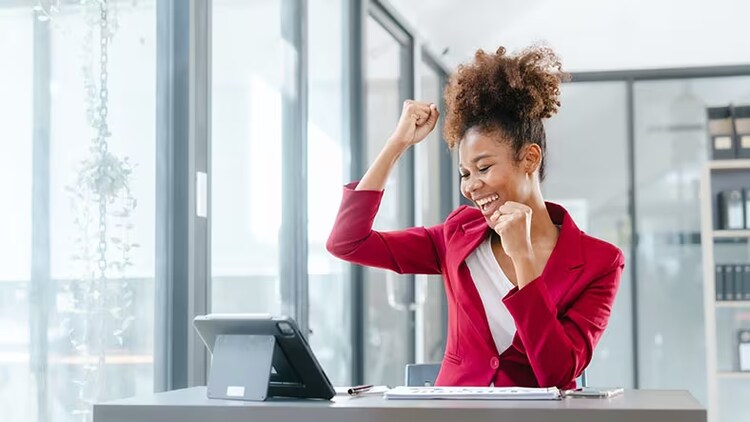 Employee portal: woman celebrating at her desk while looking at a tablet