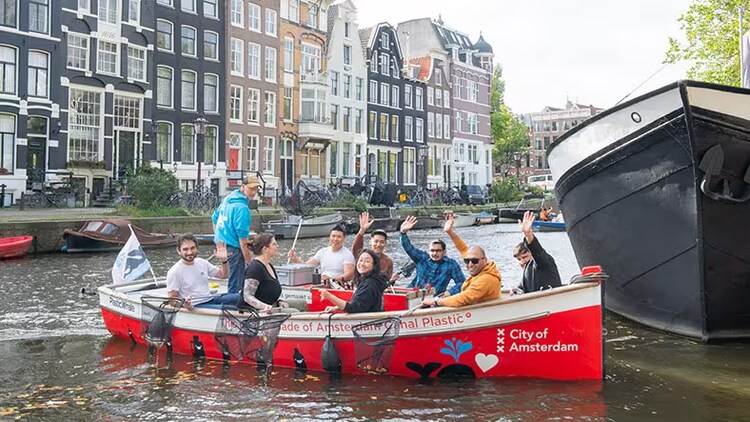 ServiceNow employees holding nets over the side of a boat in an Amsterdam waterway