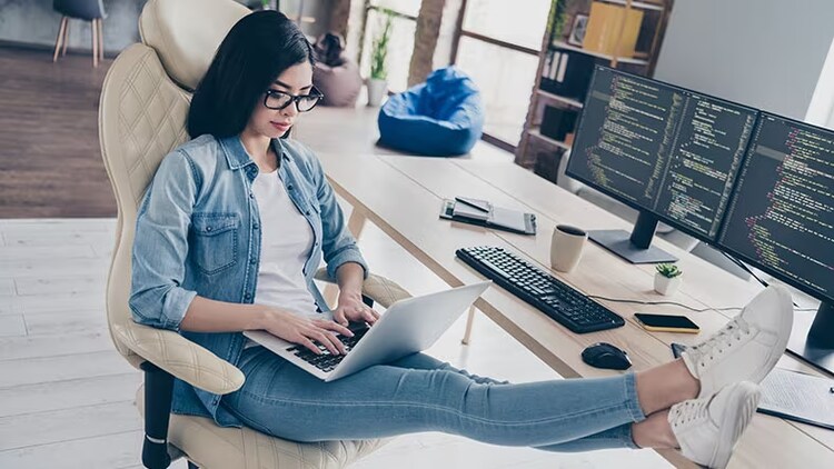 Skilled tech workers: female typing on laptop with feet on desk where two computer monitors display code