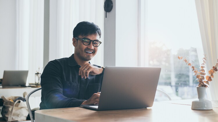 No-code platform: man sitting at a desk in front of a window, smiling at his open laptop